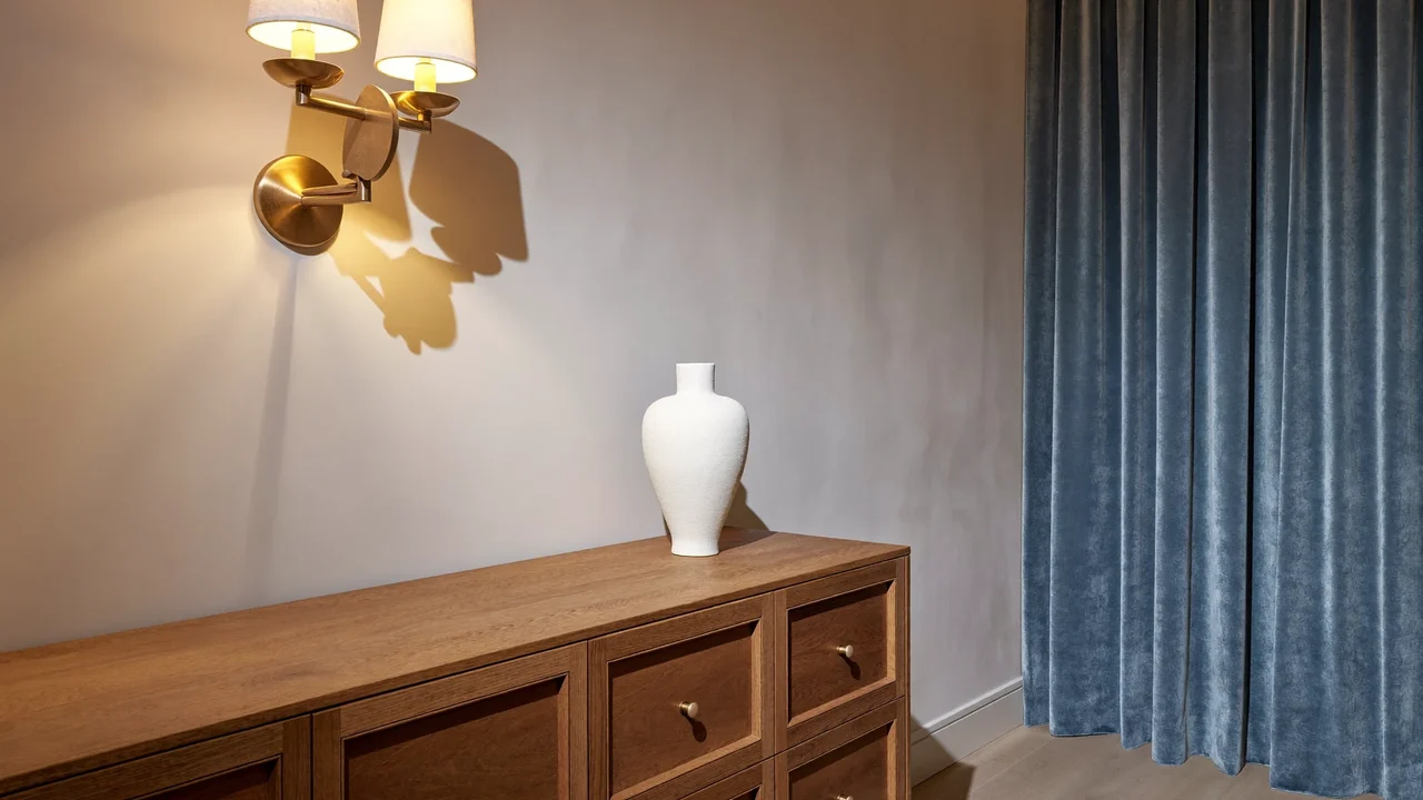 Detail einer fertigen Raumecke mit Putzwand, Messingleuchte, Samtvorhang und Eichen-Sideboard mit Vase